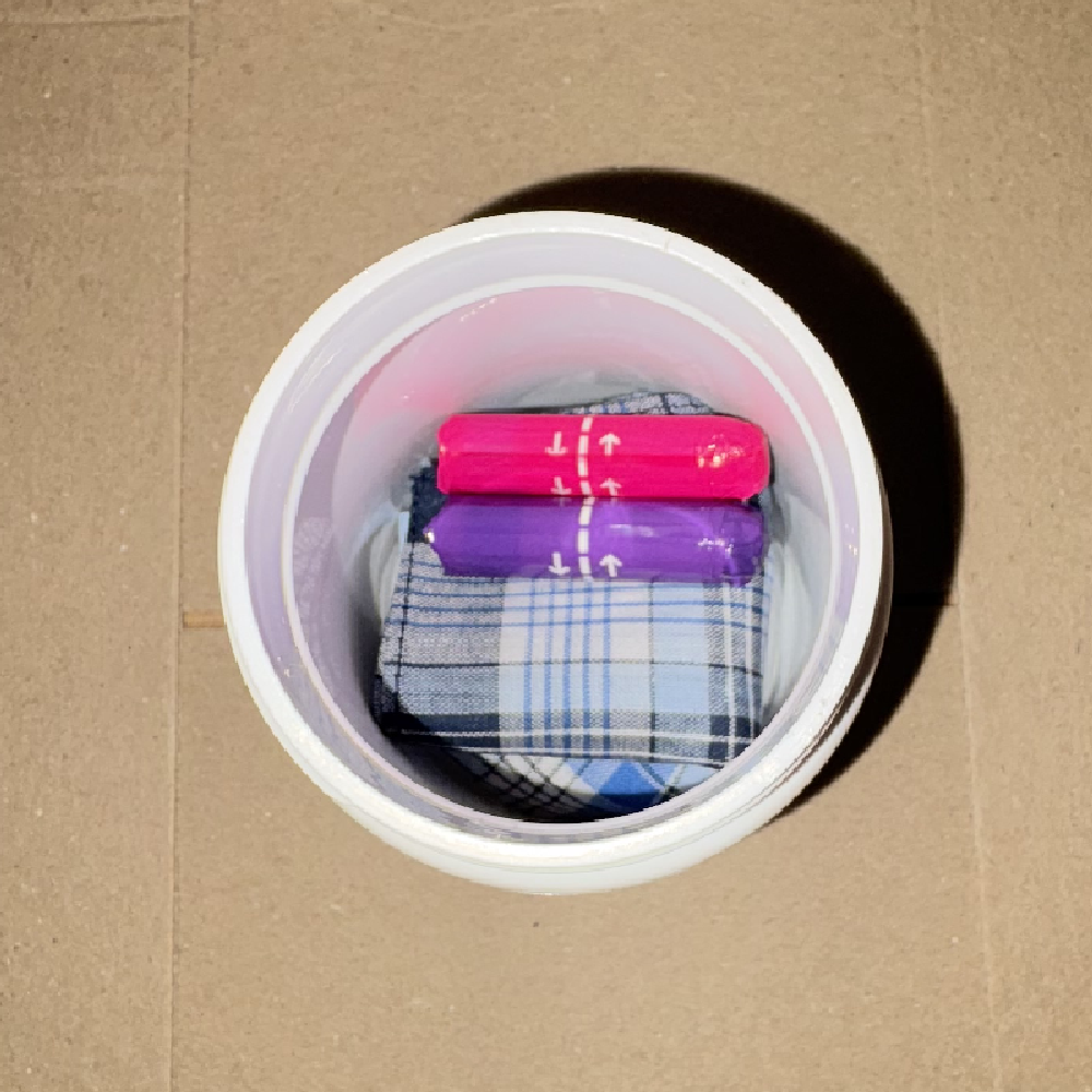 Two tampons, one pink and one purple, stacked on top of a folded handkerchief inside the capsule tub.