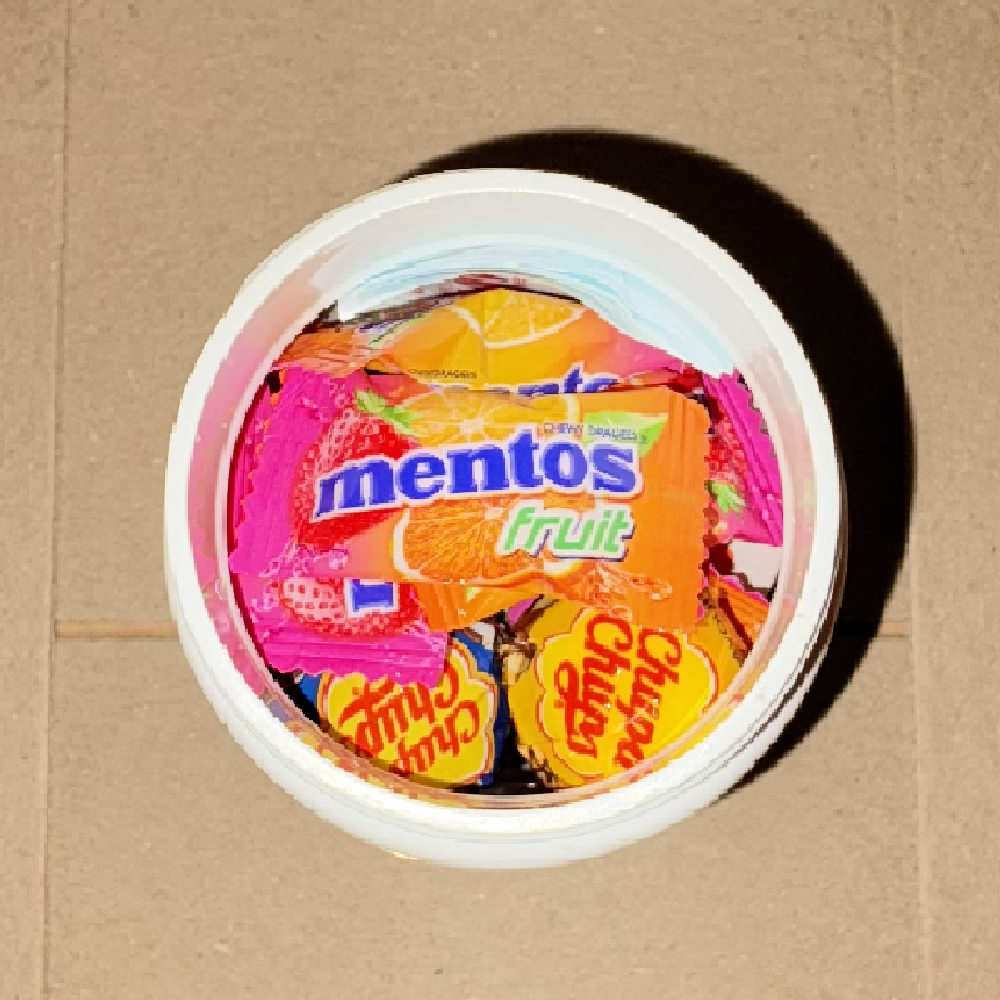 Mentos fruit chews and lollipops filling the upper layer of the capsule tub.