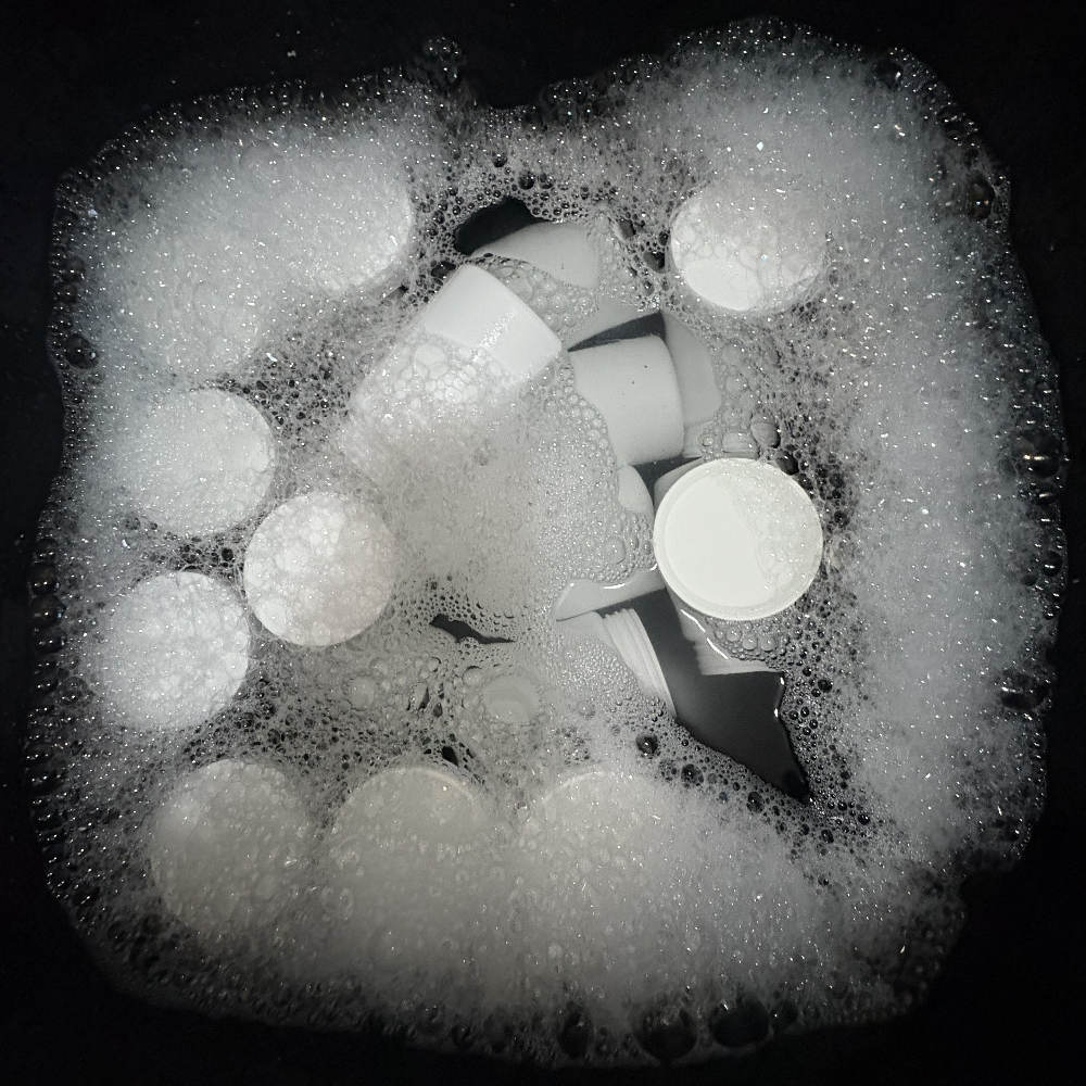 Hand scrubbing a container with a sponge and biodegradable soap.